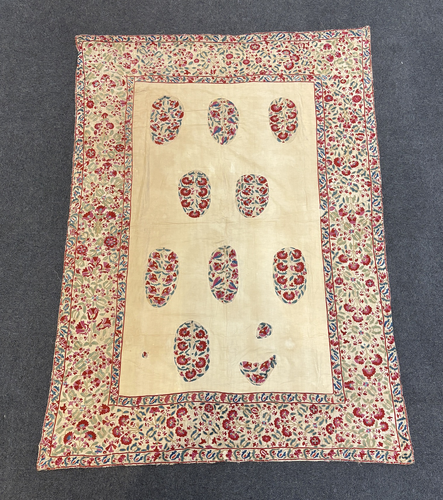 A mid to late 19th century Uzbek Suzani, embroidered in hand dyed silks with a symbolic floral and foliate design as wide border, the central panel has been recovered, only revealing a few spot motifs of the original emb